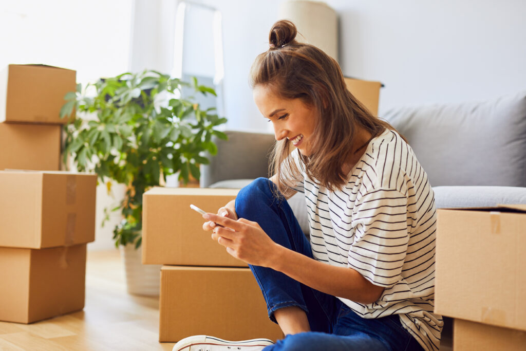 Frau mit Handy in der Hand. Hintergrund: Umzugskartons