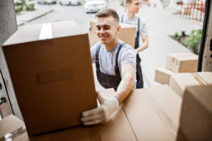 A young handsome smiling mover wearing uniform is reaching for t