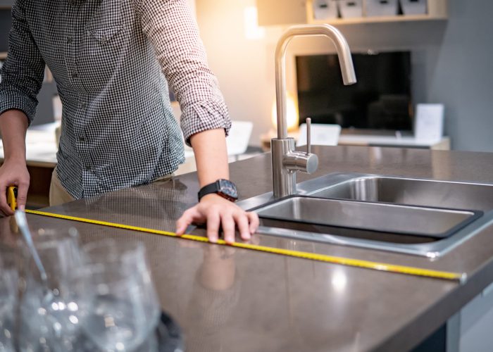 Young Asian man using tape measure for measuring granite countertops on modern kitchen counter in showroom. Shopping furniture for home improvement. Interior design concept