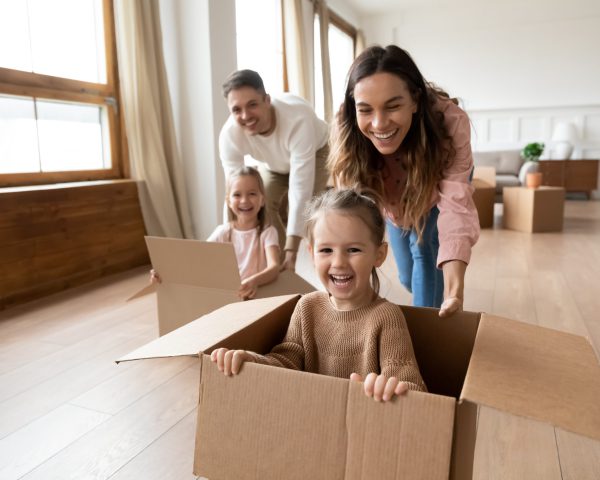 Glückliche Familie die Umzugskarton durch die Wohnung schiebt.