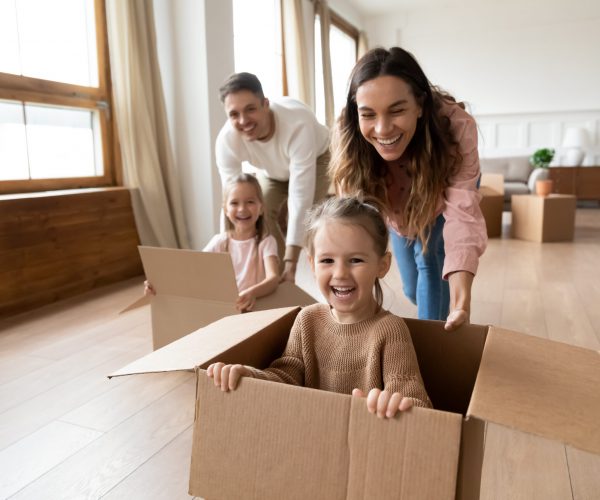 Glückliche Familie die Umzugskarton durch die Wohnung schiebt.